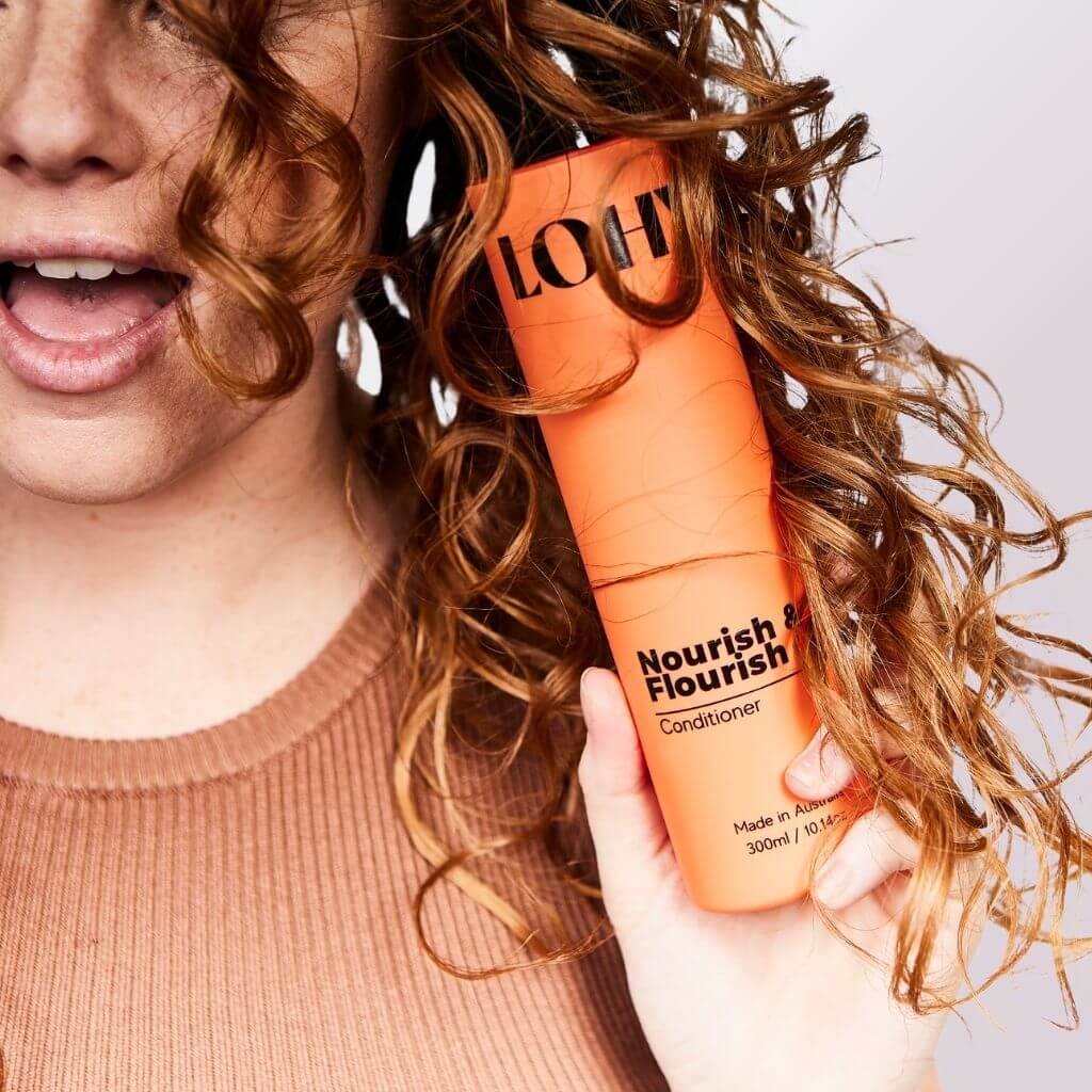 Red head holding curl conditioner bottle near her face