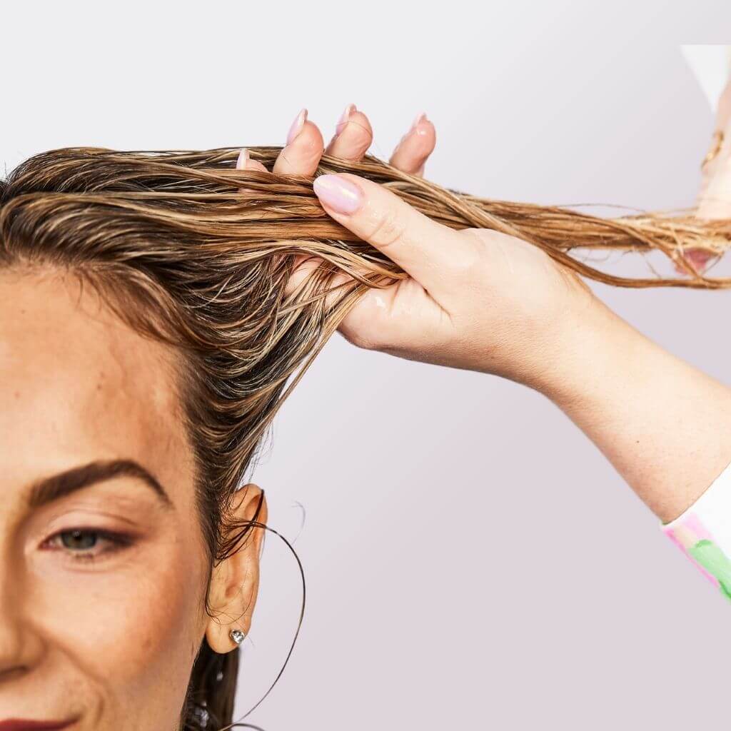 Blonde curly girl having her hair hydrated with a leave-in conditioner treatment