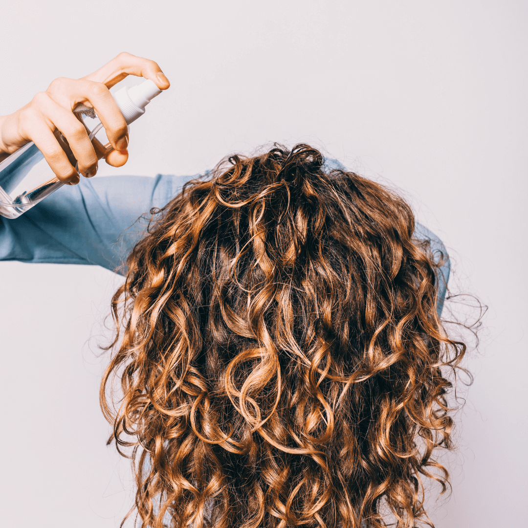 woman spraying product in long curly brunette hair