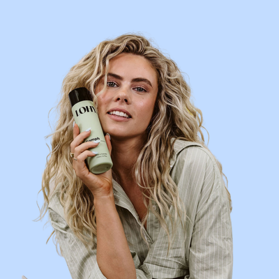 blonde wavy haired woman holding LOHY. oomph hydrating gel while smirking at viewer